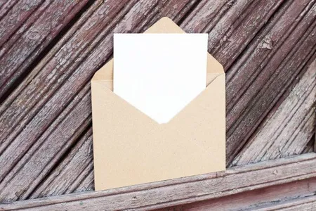 Ein geöffneter Briefumschlag mit einer Karte darin, vor hölzernem Hintergrund. Das soll das E-Mail-Symbol symbolisieren.