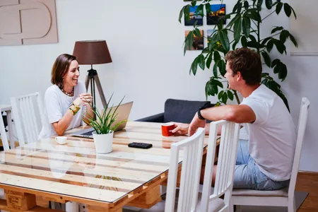 Anja und Axel lachen am Tisch bei Kaffee und Laptop.
