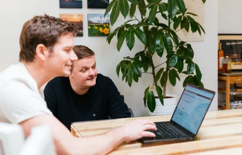 Axel und Christian betrachten ein CRM aus Deutschland im Büro am Laptop.
