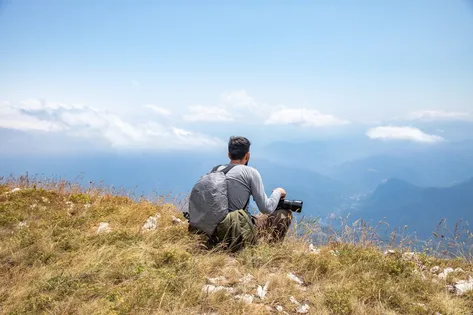 Mann mit Kamera blickt vom Berg ins Tal.