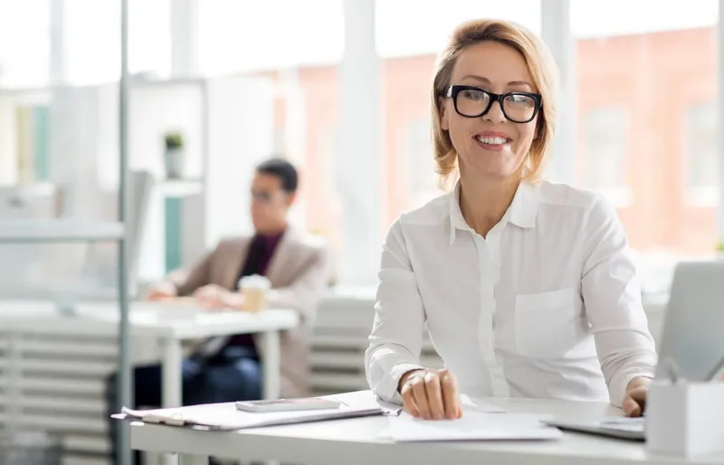 Geschäftsfrau arbeitet am Laptop, im Hintergrund ein Mitarbeiter.